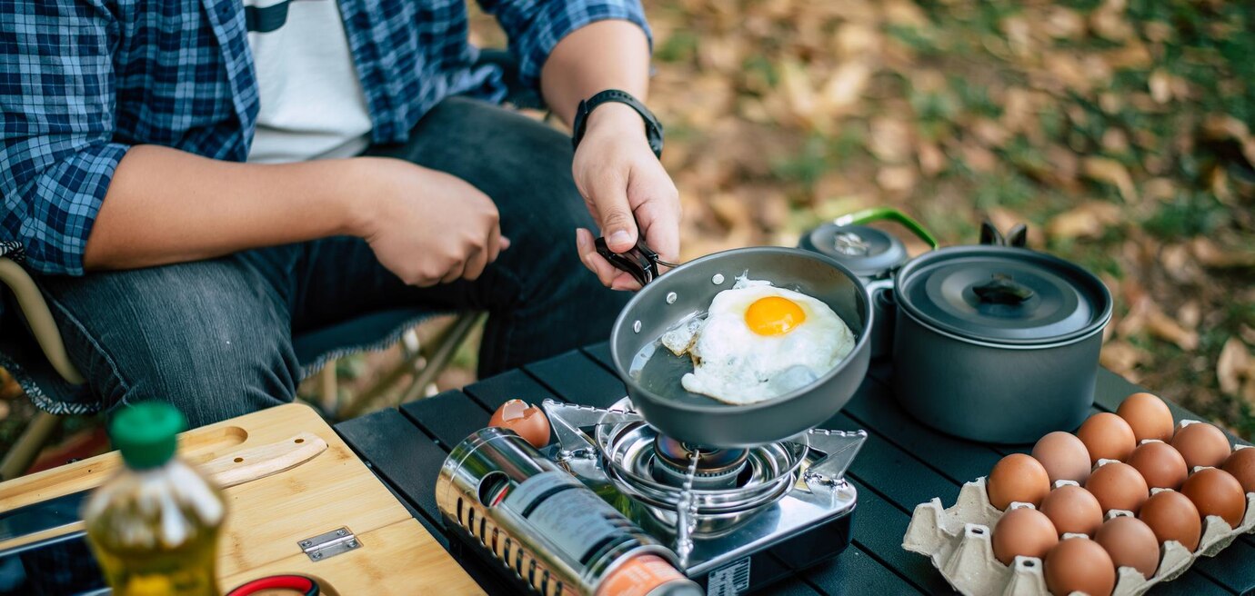 Voorkant -NL Kampeeruitrusting Verkoop 2024 portrait asian traveler man glasses frying tasty fried egg hot pan campsite outdoor cooking traveling camping lifestyle concept 1150 61557
